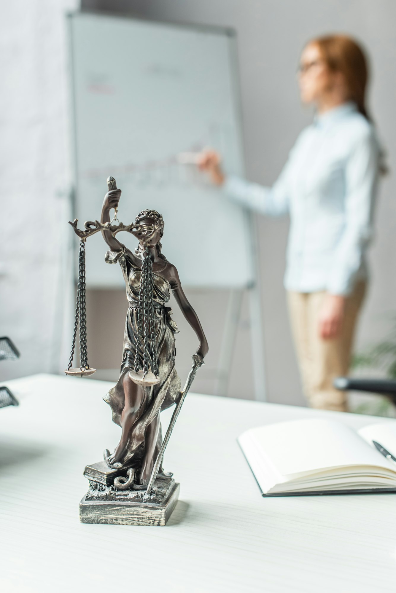 Themis figurine on workplace with blurred female lawyer on background